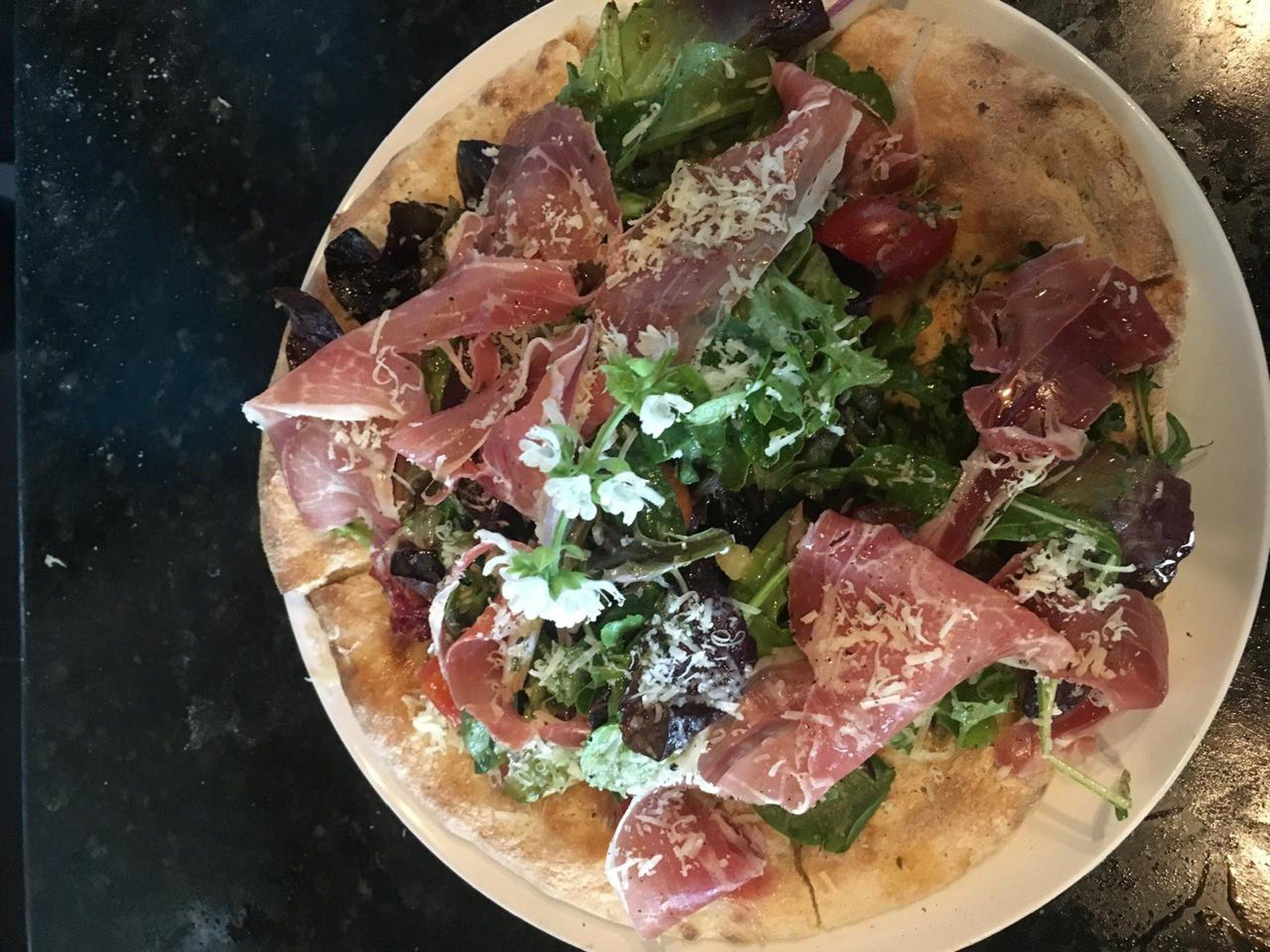 La primera ensalada Giorgio, sobre base de masa horneada con prosciutto, lechugas, tomate cherry y parmesano, frente al horno de leña de Santo Olivo